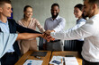 © Prostock-studio - Group of diverse colleagues in a corporate office come together to celebrate their success by stacking hands. This moment showcases unity and collaboration among team members during a meeting.