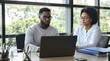 © Khalid Ghurafa - Two colleagues collaborating on a laptop in a modern office setting.