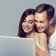 © vgstudio - Image of expressive happy smiling cute couple using laptop notebook together, isolated grey gray background. Internet search, shopping, online store concept - man woman with computer. Square
