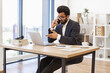 © sofiko14 - An Arab businessman wearing glasses is talking on the phone while working on his laptop in the office