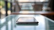 © NoorArt Studio - A silver smartphone on a reflective glass table in a blurred indoor setting