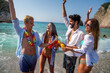 © NDABCREATIVITY - Group of young friends enjoying summer beach vacation with drinks on a tropical coastal destination