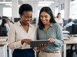 © Marko - Two happy busy professional business women, diverse female employees workers talking using digital tablet device working together in partnership
