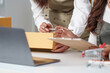 © Natee Meepian - E-commerce collaboration. Women discussing order details while managing packages and a laptop.