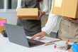 © Natee Meepian - E-commerce teamwork. Two women collaborating on online order fulfillment with packages and laptop.