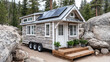 © Katerina Bond - Tiny house with solar panels nestled in forest setting, surrounded by rocks and trees, representing sustainable off-grid living and eco-friendly minimalist lifestyle.