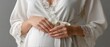© pvl0707 - Close-up of a pregnant woman's belly with hands on stomach in a white robe against a soft background with natural lighting