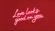 © Wishi - A neon sign with pink glowing text that reads love looks good on you on a red background with a romantic ambiance and a stylish typographic