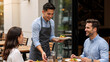© Vyatcheslav - Smiling waiter serving food to a happy couple at an outdoor restaurant table. Professional hospitality and dining concept