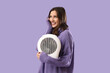 © Pixel-Shot - Young woman with electric fan heater on lilac background