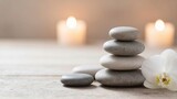 A calming arrangement of stacked stones and an orchid flower beside softly glowing candles.