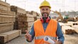 © Vasiliy - A smiling construction worker in a hard hat holding a blueprint. Professional male engineer standing at an industrial lumber yard