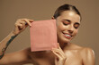 © Valerii Apetroaiei - Smiling woman showing pink facial sheet mask on beige background