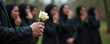 © IvaNad - man in black holds a white rose against a background blurred by grieving people, close-up