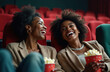 © Vadym - Two Black women laugh heartily in movie theater seats. Friends share popcorn bucket, enjoying comedy film. Happy romantic leisure time watching movie together, cheerful smiles.