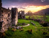 Ancient castle ruins framed by a sunset sky, with a green valley