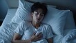 © Vadym - Young Asian man sleeps restlessly in bed at night. He appears troubled, potentially experiencing a nightmare or sleep disorder. The dim lighting creates a somber mood.