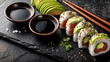 © Yurii Semonov - Overhead view of sushi rolls with avocado slices and soy sauce on dark slate