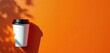 © Pete - White disposable coffee cup with black lid rests on bright orange background with leaf shadows. Take away hot drink for morning commute. Lifestyle flat lay header.
