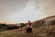 © Cavan Images - Woman and daughters in flowing dress cuddling on sandy path at dusk