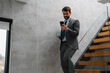 © Novak - Young businessman using smartphone while walking down stairs with laptop.