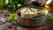 © AndiAzis - Canned tuna with herbs in a round metal container on rustic wooden surface, garnished with chopped green herbs and fresh dill, with a blurred natural background
