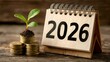 © CHAIYAPHON - In 2026, a young plant grows from coins suggesting financial growth, investment, and prosperity in the new year on a wooden background.