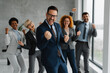 © Novak - A diverse team of successful professionals smiling and making positive hand gestures in a modern office. Concept of victory, great teamwork, and corporate success.