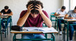 © NeuroCake - Stressed male student taking a difficult exam in a classroom. Anxious young man with his head in his hands feeling academic pressure during a test