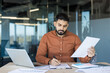 © Liubomir - Businessman focused on reviewing and signing contract documents at a modern office desk with laptop and paperwork, conveying professional responsibility, negotiation and career-focused determination