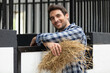 © auremar - positive man feeding horses with hay at stable