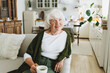 © shurkin_son - Happy relaxed confident old lady in stylish cardigan enjoying her coffee and retirement relaxing in sofa on sunday holding white mug with hot drink and looking at camera with smile