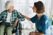 © shurkin_son - Female nurse in blue uniform cheering up her elderly disabled female patient in wheelchair, touching gently her shoulder, expressing support and giving hope to recover after rehabilitation treatment