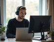 © Viktor - Man works on laptop with two monitors and headphones. He is focused on computer screen in home office setup. Casual entrepreneur works remotely using tech gadgets, concentrated on online job.