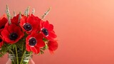 Beautiful bouquet of bright red anemone flowers with dark centers and green foliage against a peachy gradient background.