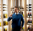 © BGStock72 - Man holds glass of wine in a wine rack room while dressed in a suit