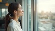 © Maryna - Woman looks out office window at cityscape sunset. Pensive female contemplates success, career goals, business future, inspiration, planning new ideas. Modern bright workspace interior.