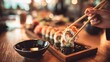 © Plaifah - Hand Holding Chopsticks with Delicious Sushi Roll Near Soy Sauce Bowl on Wooden Table in Vibrant Restaurant Setting with Soft Lighting