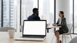 © Roushon - An open laptop mockup sits on an office table during a business discussion in a modern office setting