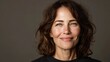 © Newleks - Middle aged woman with brown curly hair and green eyes smiling, her genuine expression conveying natural beauty, confidence, and graceful aging in a headshot against a neutral background