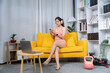© Kritdanai - Home Fitness Routine: A woman embraces a fitness routine at home, lounging on a vibrant yellow sofa, engaging with technology, and preparing for her workout.