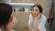 © tol_u4f - Woman applies yellow eye patches while looking in the bathroom mirror during a skin care routine in a modern home setting