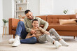 © Pixel-Shot - Happy father having fun with his son on floor near brown leather sofa at home