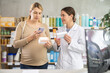 © JackF - Interested expecting mother scanning QR codes on supplement boxes at drugstore, comparing two products, while smiling female pharmacist explaining benefits for fetal development