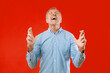 © Prostock-studio - A man in a blue checkered shirt shows a clear sign of frustration. He raises his hands and tilts his head back. The background is a solid red color. The setting is simple and direct.