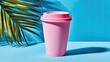 © alap - Pink disposable cup with lid casts a shadow next to a palm leaf.