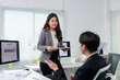 © amnaj - Young Asian businesswoman presenting sales report results on a computer screen to a male colleague in a modern office setup