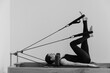 © Anton - Black and white photo of a slim European woman in black workout clothes performing different positions on a Pilates reformer machine showing professional training, fitness, and body control