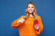 © ViDi Studio - Young happy smiling cheerful Caucasian woman wear yellow sweater casual clothes hold in hand use mobile cell phone show thumb up isolated on plain blue background studio portrait. Lifestyle concept.