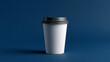 © MDALI - A minimalist studio photograph depicts a tall, smooth, logo-free white disposable paper coffee cup with a dark gray plastic lid. It is centered against a deep blue background on a flat surface.